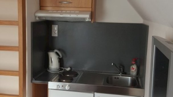 Pohľad od postele jednoizbového apartmánu na poschodí, časť kuchynskej linky, rebrík do podkrovnej  časti, televízor