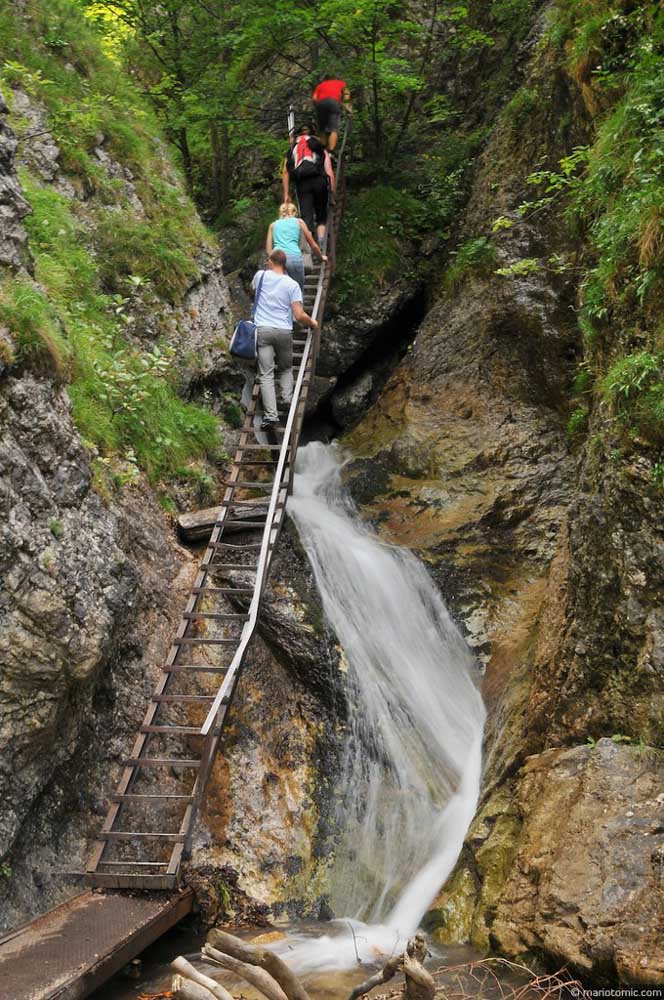 Turisti kráčajú po rebríku pomedzi skaly na Jánošíkových dierach