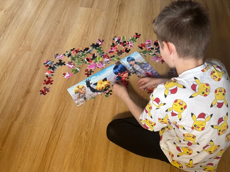 Chlapec na drevenej podlahe skladá puzzle.