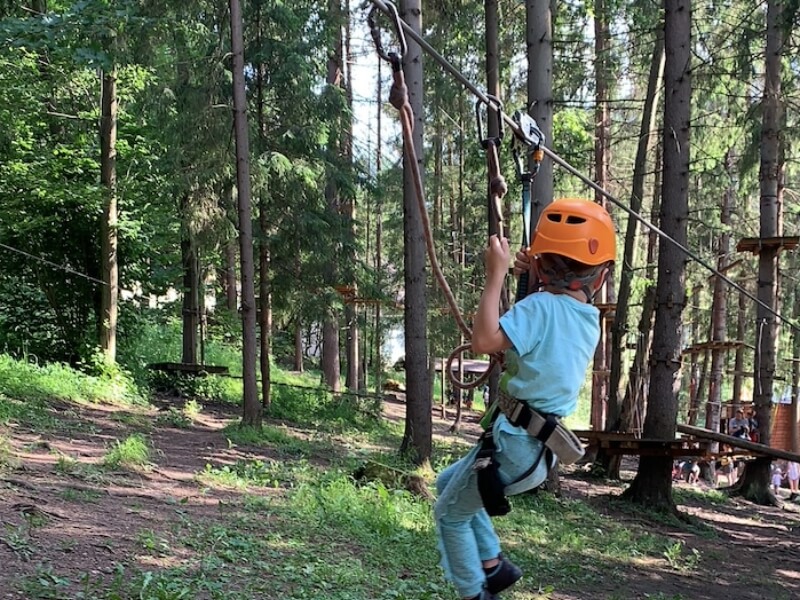 Malý chlapec s oranžovou prilbou v sedáku v lanovom parku.