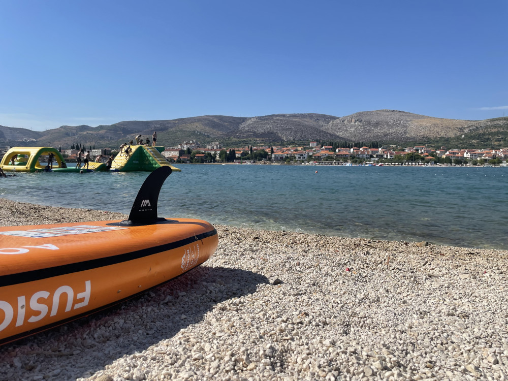Oranžový paddleboard položený na brehu mora na kamienkovej pláži.