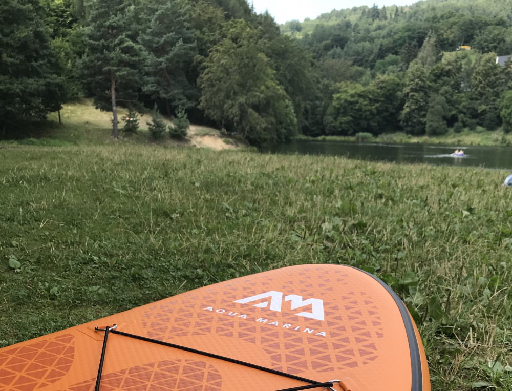 Paddleboard položený na tráve pri stromoch na brehu štiavnického tajchu.