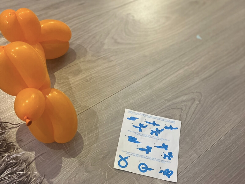 Oranžový balón v tvare zvieratka na podlahe s návodom ako ho poskladať.