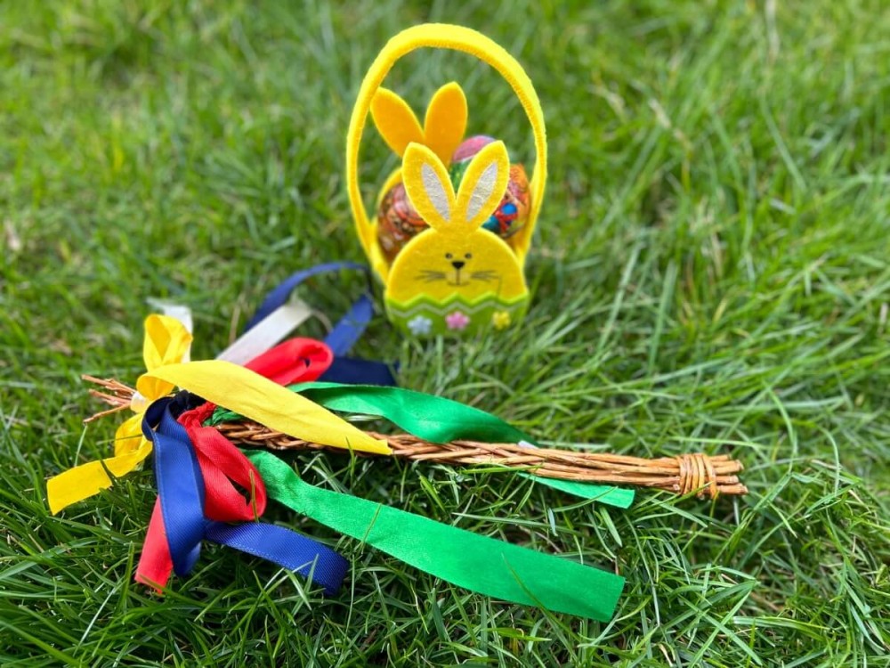 Žltý košík s motívom zajačika naplnený kraslicami a veľkonočný korbáč