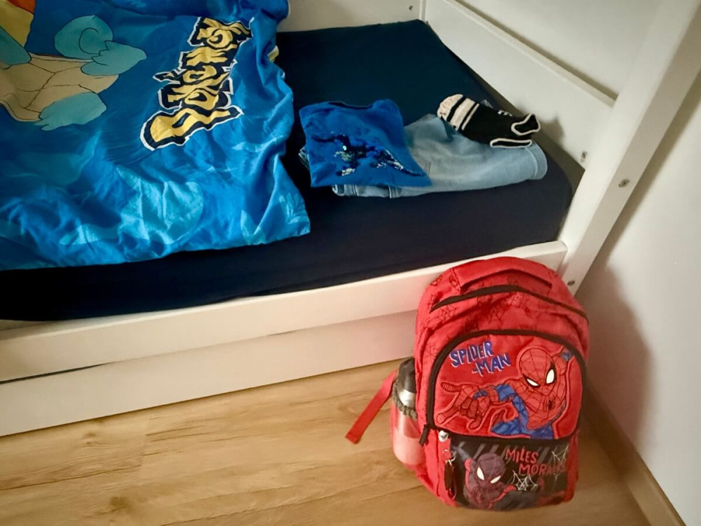 Nachystaná školská taška pri chlapčenskej bielej posteli.